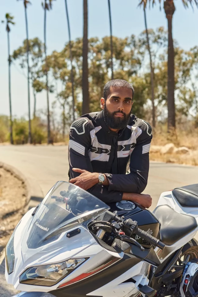 Motorcycle lifestyle dating photo for men in Los Angeles, man in riding gear leaning on a white sport bike on a palm-lined road, adventurous online dating profile image.