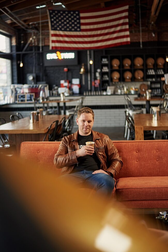 Coffee shop lifestyle dating photo for men, casual seated portrait with coffee for online dating profiles, natural image for Hinge, Bumble, Tinder, and matchmaking platforms
