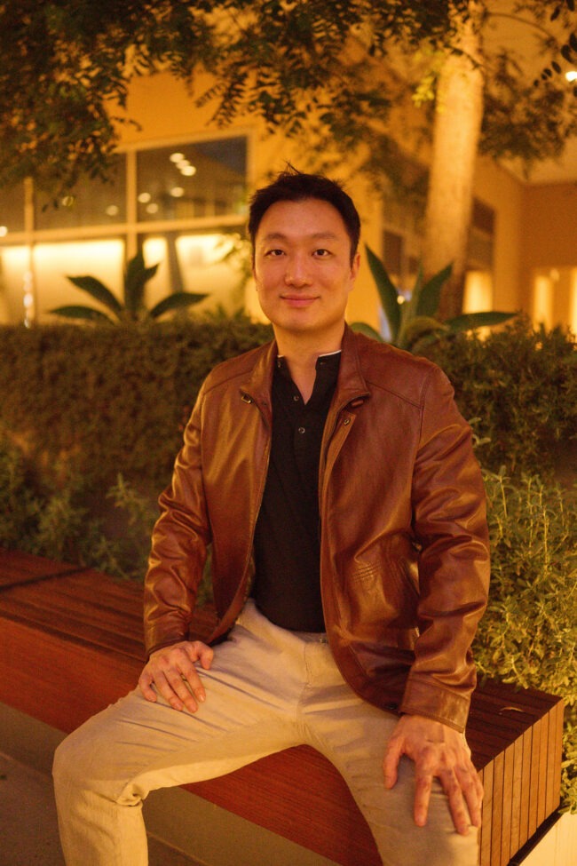 Man wearing a brown leather jacket in a nighttime outdoor dating profile photo.