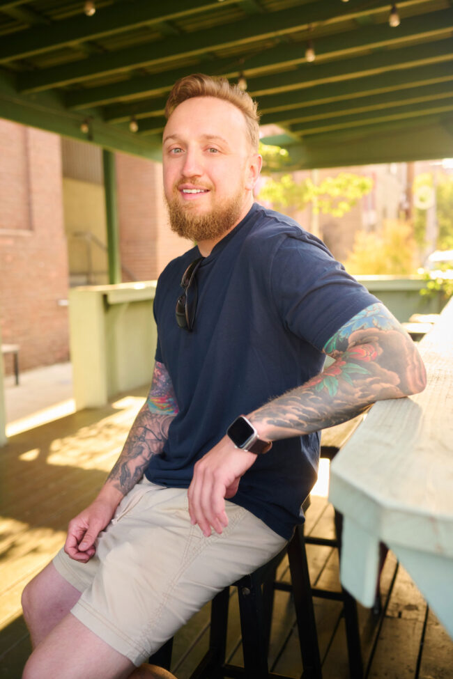 Man wearing a navy T-shirt and khaki shorts in a relaxed outdoor dating profile photo.