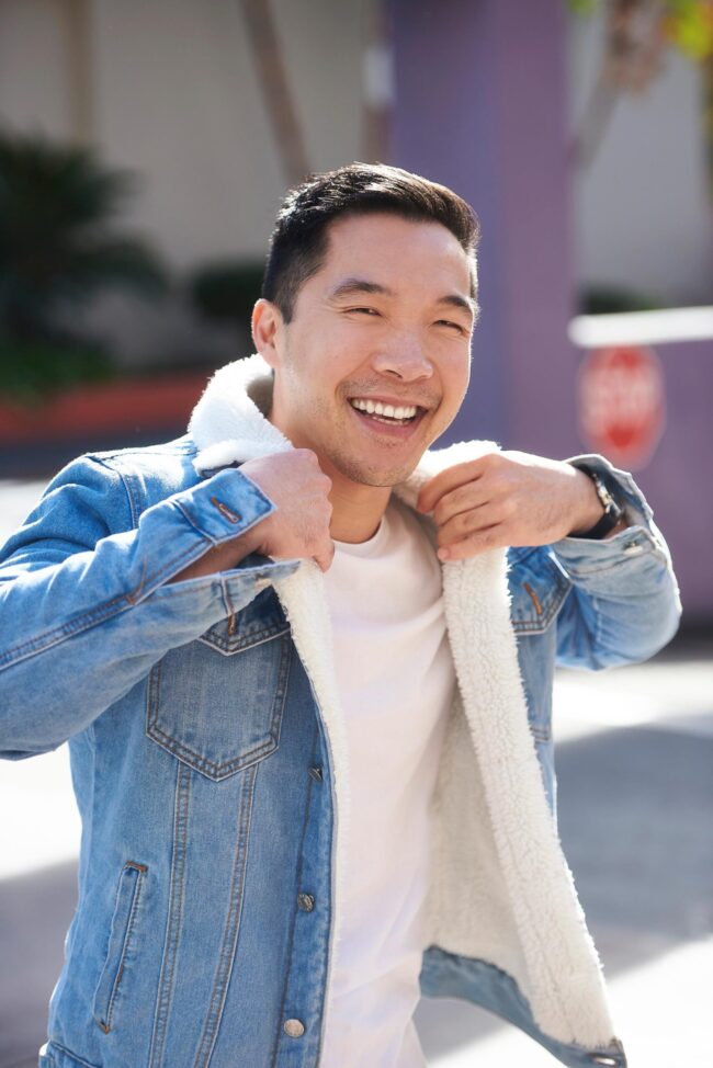 Man smiling in a denim jacket and white T-shirt for a casual outdoor dating profile photo.