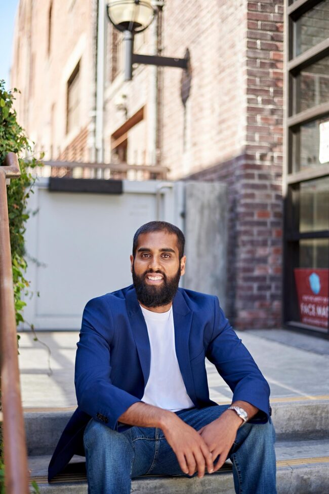 Man wearing a blue blazer, white T-shirt, and jeans while sitting outdoors for a dating profile photo.