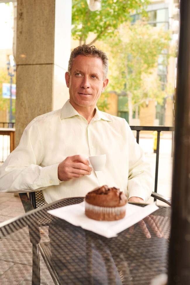 Man wearing a light button-down shirt while sitting at an outdoor cafe for a dating profile photo.