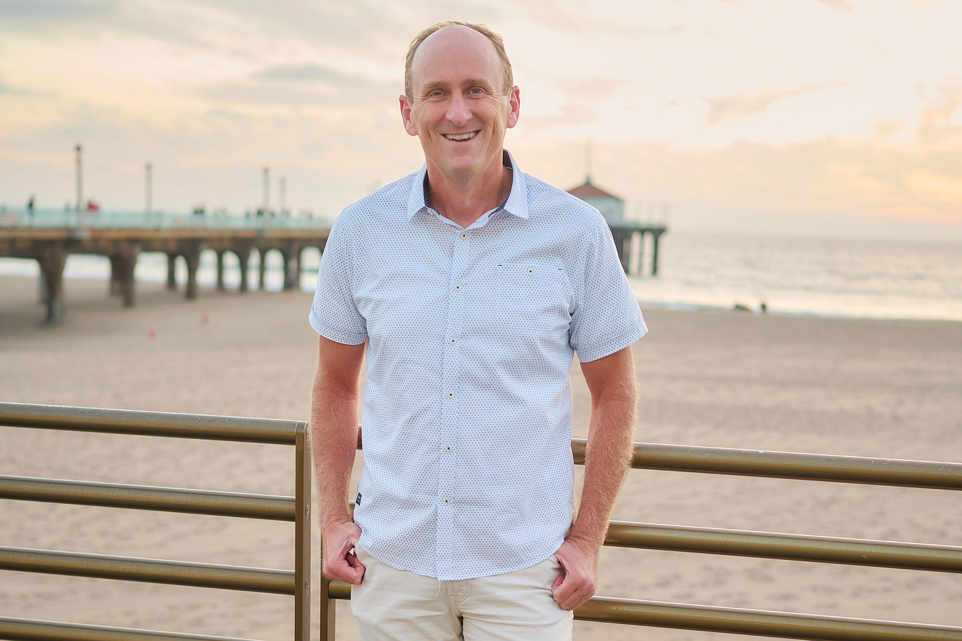 Guide for Single Men in Los Angeles Man smiling near a Los Angeles beach pier for a relaxed dating profile photo.