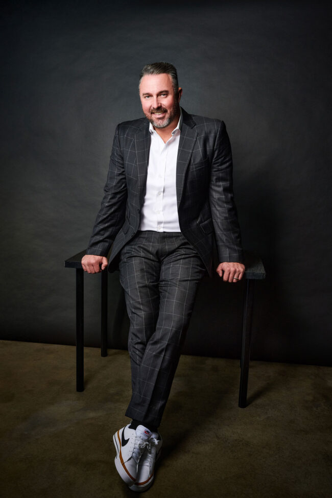 Modern executive headshot in Los Angeles, seated business portrait with dark studio backdrop, professional image for LinkedIn, company website, and executive bio