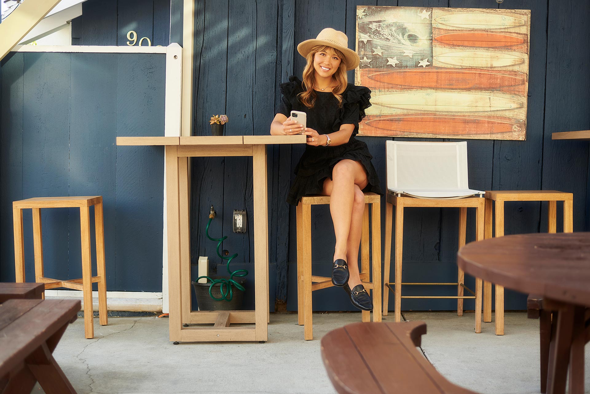 Casual Patio Meeting for First Date Length Woman sitting at an outdoor patio table, holding a phone and smiling in a relaxed cafe-style setting.