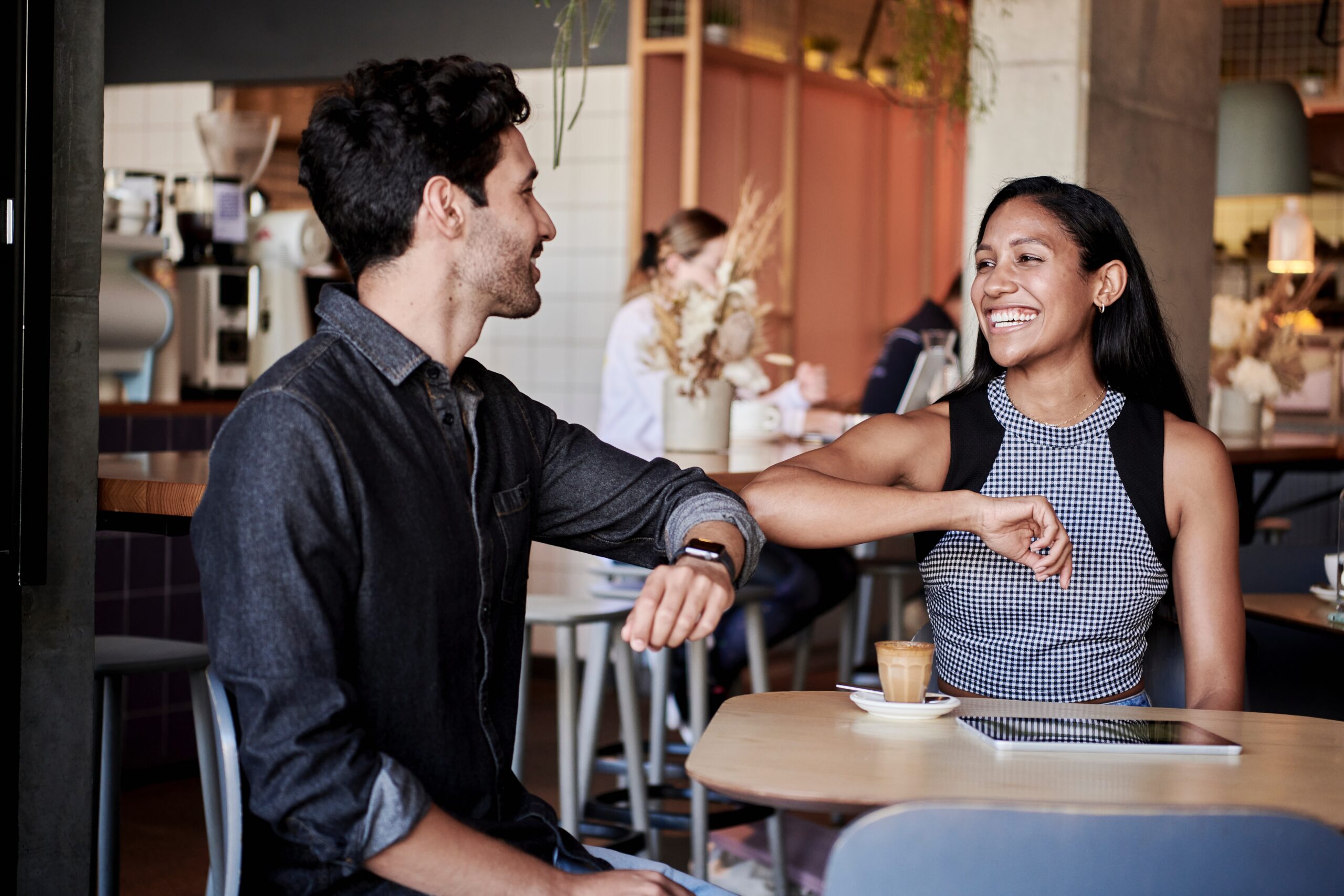 Coffee Conversation for Ideal First Date Length Man and woman smiling while talking at a cafe table with a small coffee drink and tablet on the table.