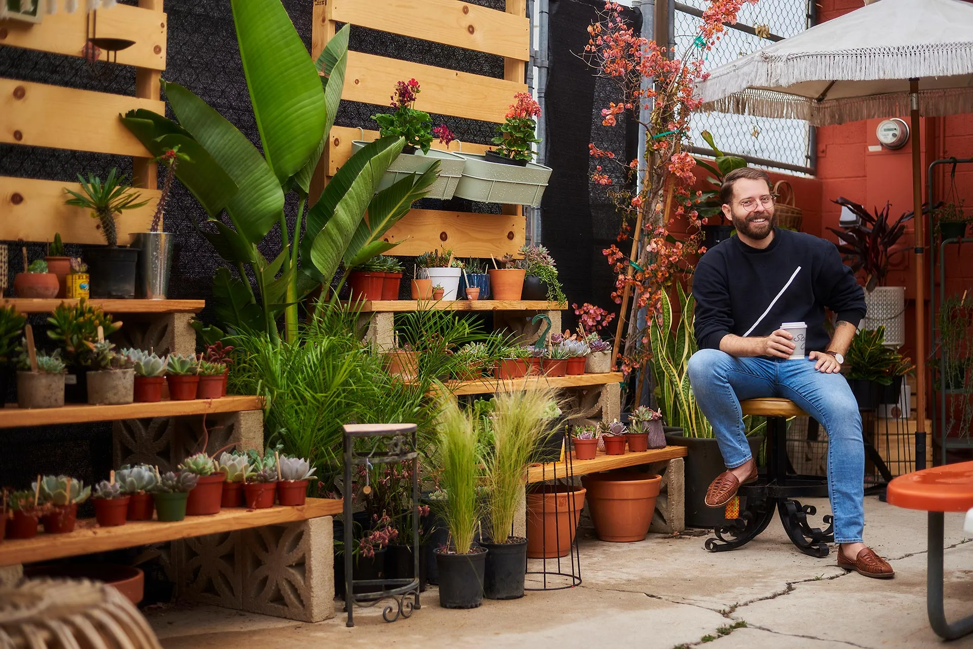 Casual Coffee Photo for Los Angeles Dating Tips Man sitting with a coffee cup in an outdoor plant-filled patio, surrounded by potted plants and casual garden decor.