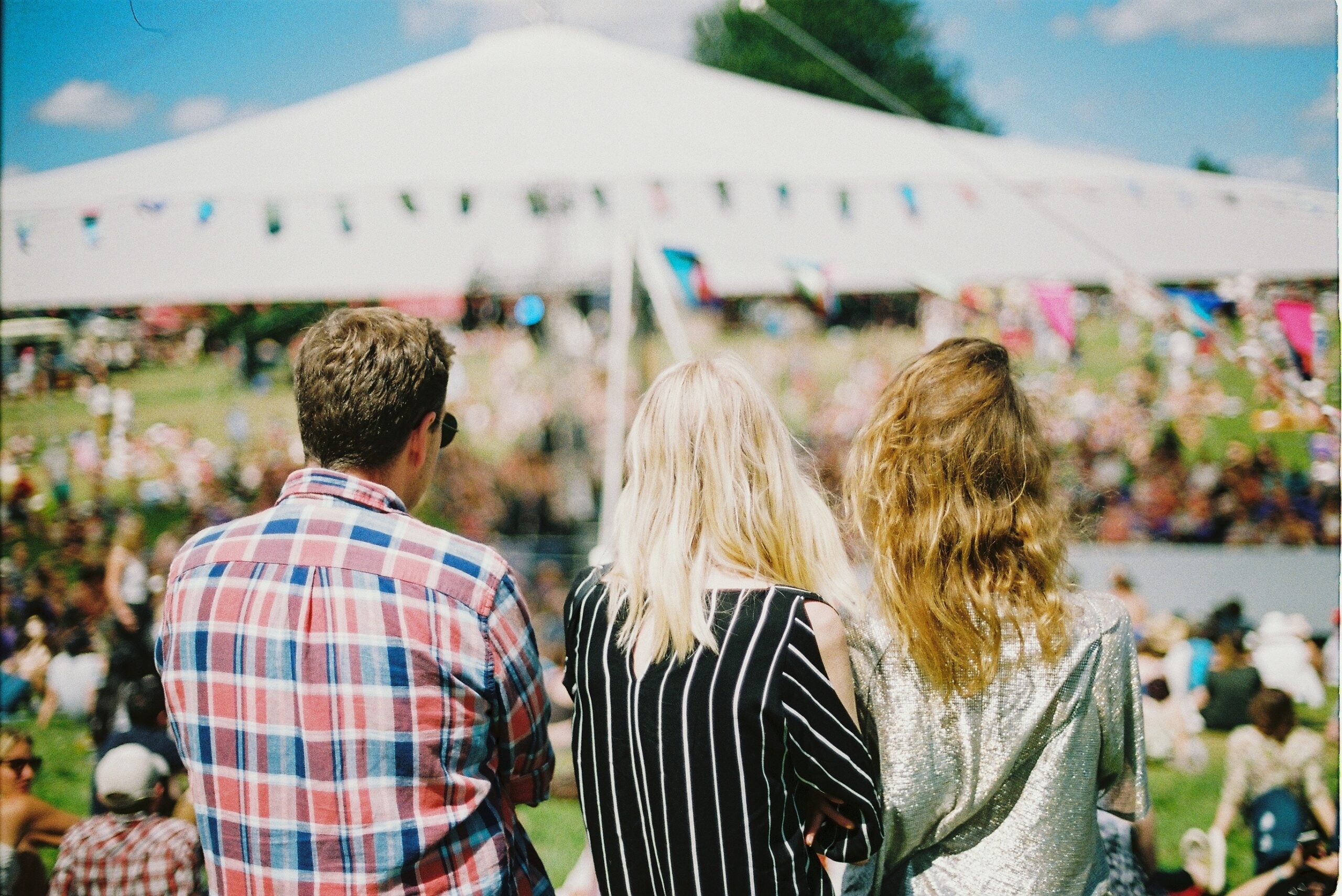 Outdoor Social Event for Single Men in Los Angeles Three people standing together at an outdoor event with a large white tent and a crowd in the background.